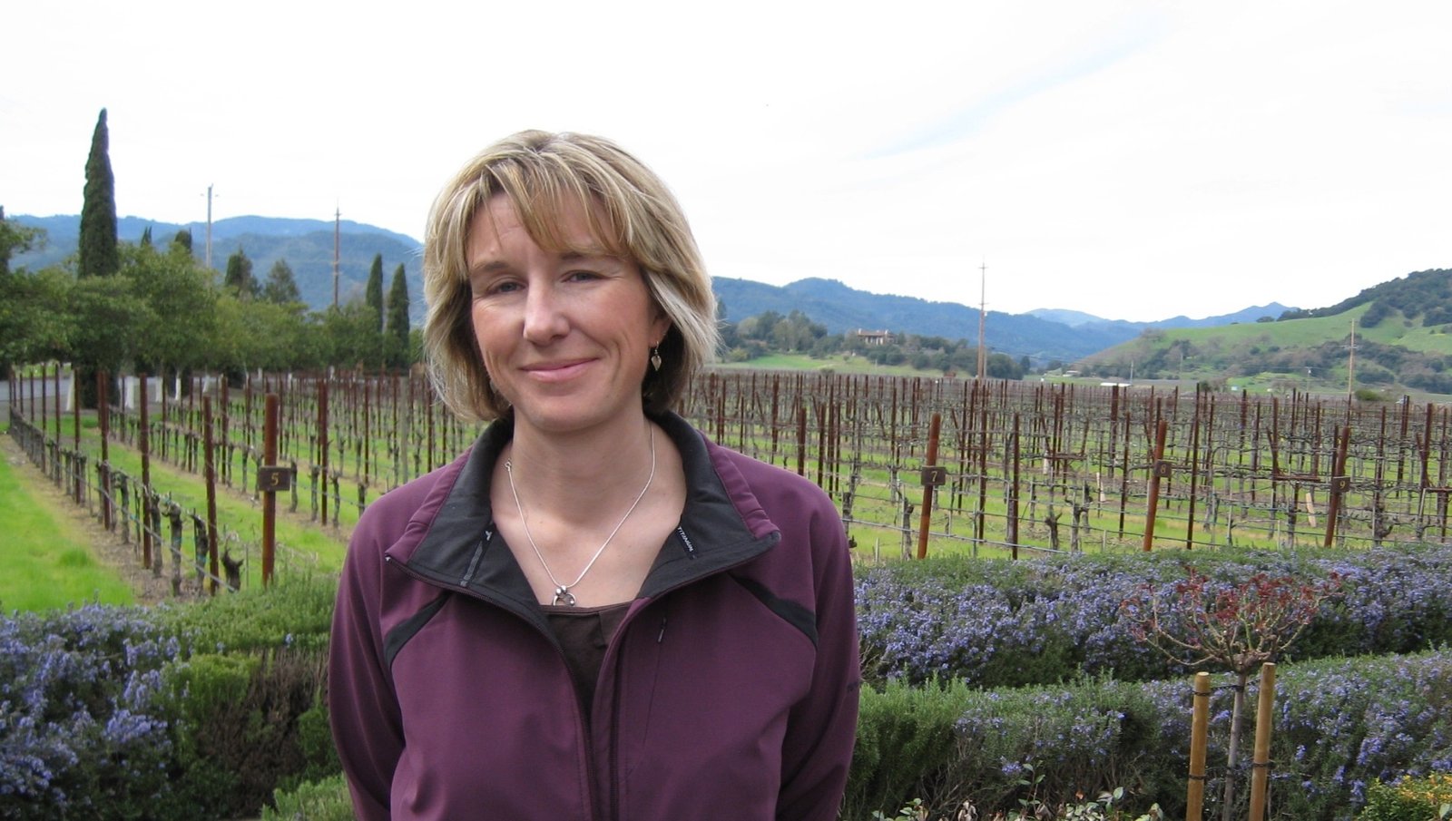 Bettina standing in a garden with vineyards and hills behind her